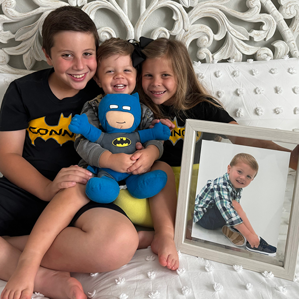 Connor's siblings wearing Connor Man shirts, cuddling with a stuffed Batman and holding a framed picture of Connor